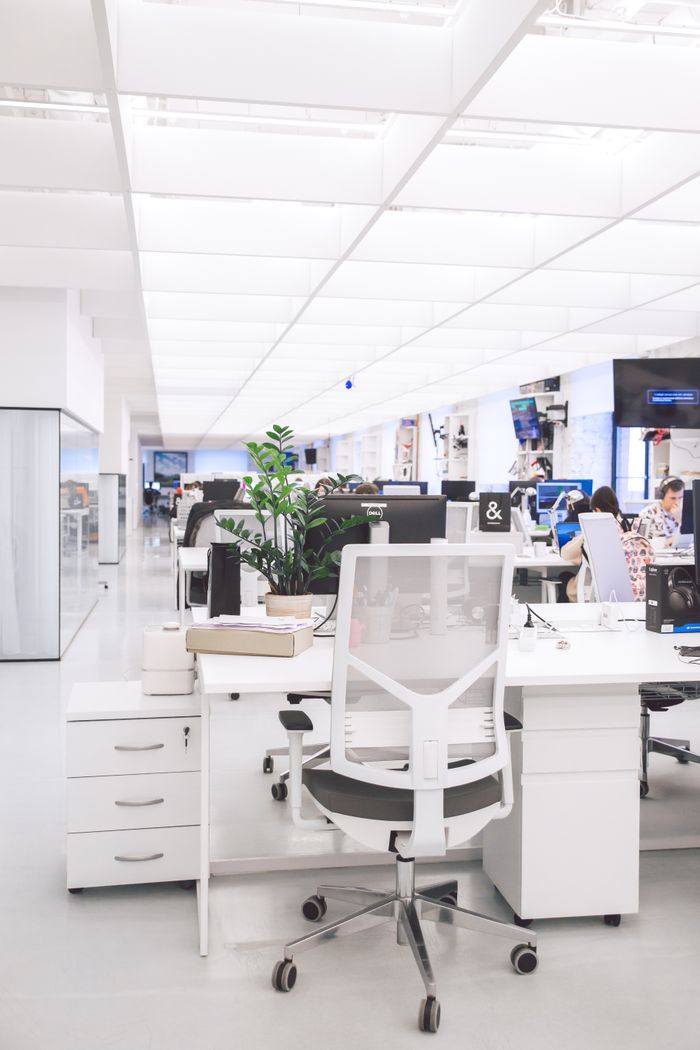 Bright modern office interior with desks, chairs, and computers in an open-plan workspace.